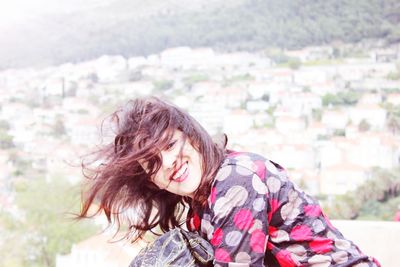 Portrait of smiling woman with messy hair against townscape