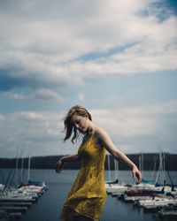 Side view of woman standing at harbor against cloudy sky