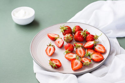 Fresh whole and sliced strawberries on a plate and sour cream in a bowl on a green background