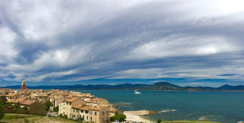 Buildings by sea against cloudy sky