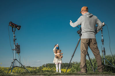 Low angle view of father photographing daughter on field