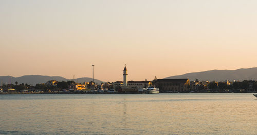 Sea by buildings against clear sky during sunset