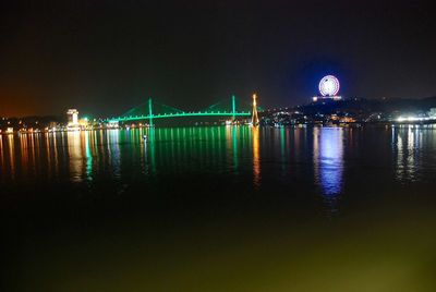Illuminated city by sea against sky at night