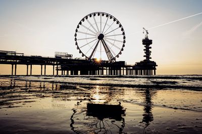 Silhouette of ferris wheel in sea at sunset