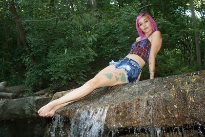 Portrait of seductive woman with dyed hair sitting on rock in forest