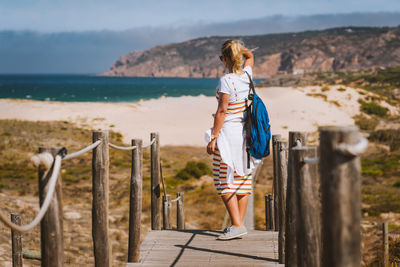 Rear view of woman standing on pier by railing against sky