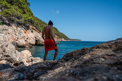 Rear view of man standing on rock by sea against sky