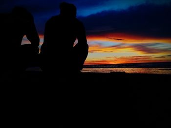 Silhouette men sitting on beach against sky during sunset