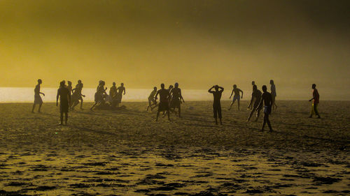 People playing soccer at beach during sunset