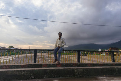 Man standing on railing against sky