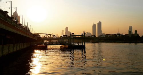 Bridge over river in city against clear sky during sunset