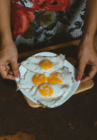 Midsection of woman holding fried eggs in plate on table