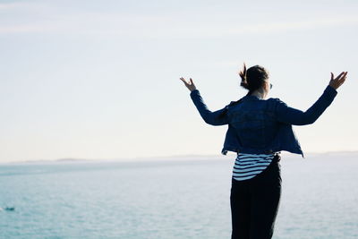 Rear view of woman with arms outstretched looking at sea against sky