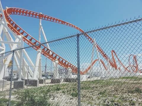 chainlink fence, metal, fence, protection, clear sky, sky, safety, grass, metallic, day, sunlight, outdoors, security, built structure, blue, leisure activity, field, amusement park, beach, nature