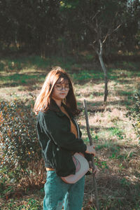 Portrait of young woman standing on field in forest