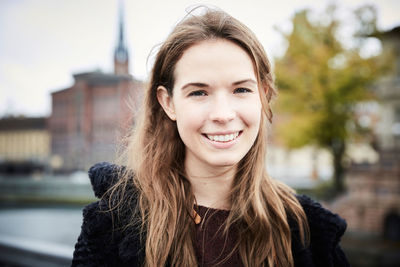 Close-up portrait of smiling young woman with brown hair in city