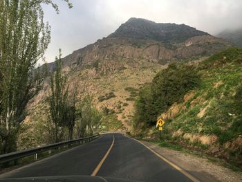 Country road leading towards rocky mountains against sky