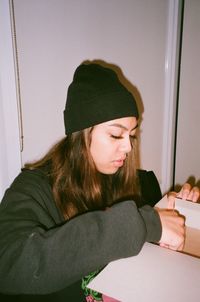 Portrait of young woman sitting against wall at home