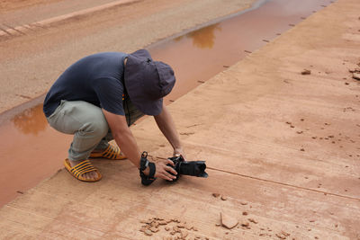A photographer stoops to take a low angle shot on a concrete road under construction.