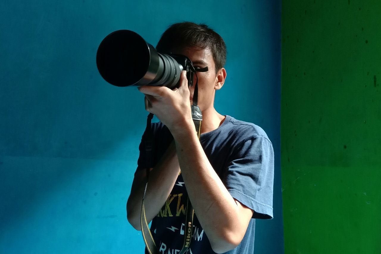 MAN HOLDING CAMERA WHILE STANDING AGAINST BLUE WALL