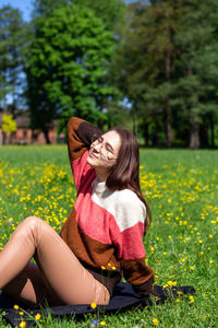 A beautiful young lady sitting on the grass enjoys life, feeling happy and relaxed in public park