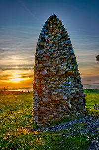 Old stone wall on field against sky during sunset