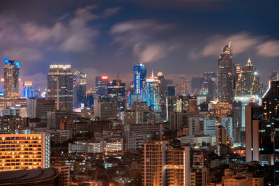 Illuminated modern buildings in city against sky at night