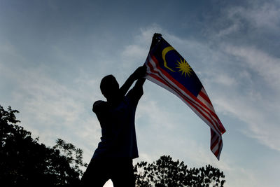 Low angle view of man waving malaysian flag against sky