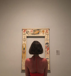 Rear view of woman standing against wall at home