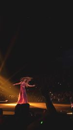 Woman by illuminated lighting equipment at night