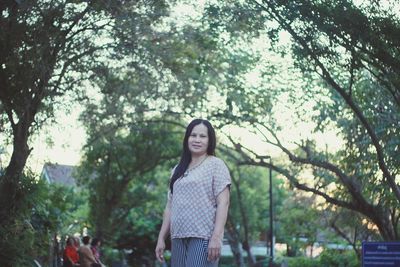 Portrait of young woman standing against trees