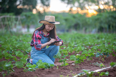 Woman using digital tablet while examining plants on agricultural field