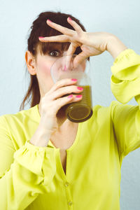 Woman having drink while standing against wall