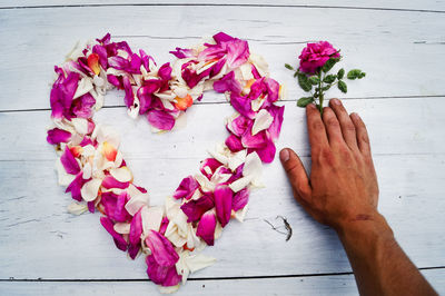 Cropped hand of man holding rose over heart shape petals at table