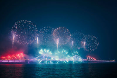 Firework display over sea against sky at night