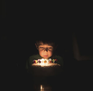 Boy blowing birthday candles on cake in darkroom