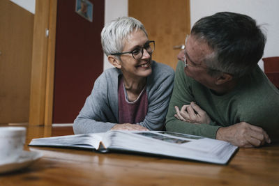 Happy senior couple lying on the floor at home with photo album