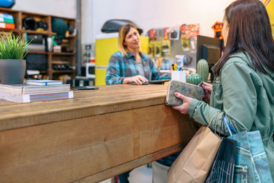 Female client taking credit card to pay purchased items while talking with woman employee on store