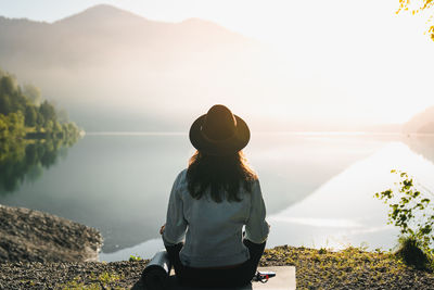 Rear view of woman sitting by lake during sunset