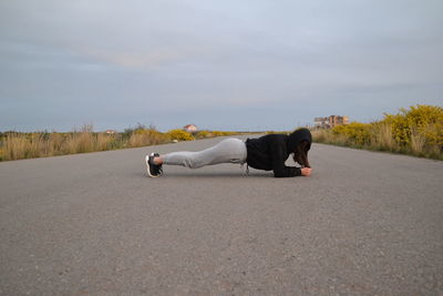 Side view of woman exercising on road against sky