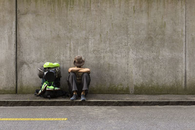 Rear view of man and woman sitting on footpath against wall