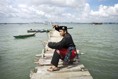 Rear view of woman sitting on boat in sea against sky