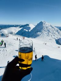 Cropped hand of man skiing on snowcapped mountain against clear blue sky