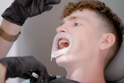 A guy with an open mouth, with braces installed, sits in an orthodontist's chair