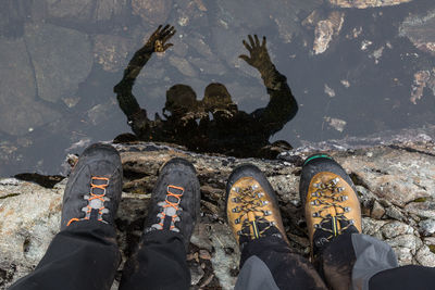 Low section of man standing on rock by water with reflection