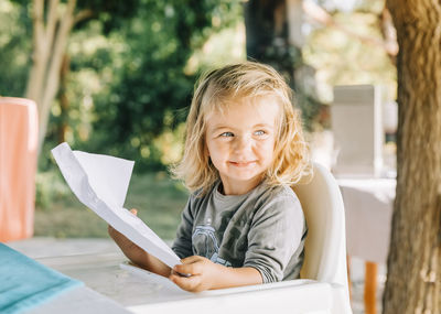 Smiling girl with paper sitting in park