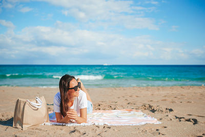 Young woman sitting at beach against sky