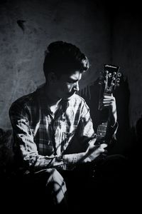 Young man holding guitar while sitting against wall