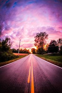 Road by trees against sky during sunset