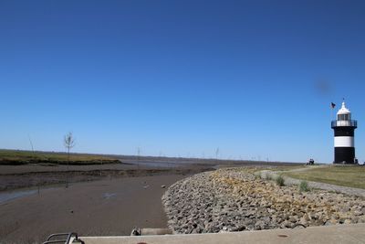 Road leading towards lighthouse on field against clear blue sky